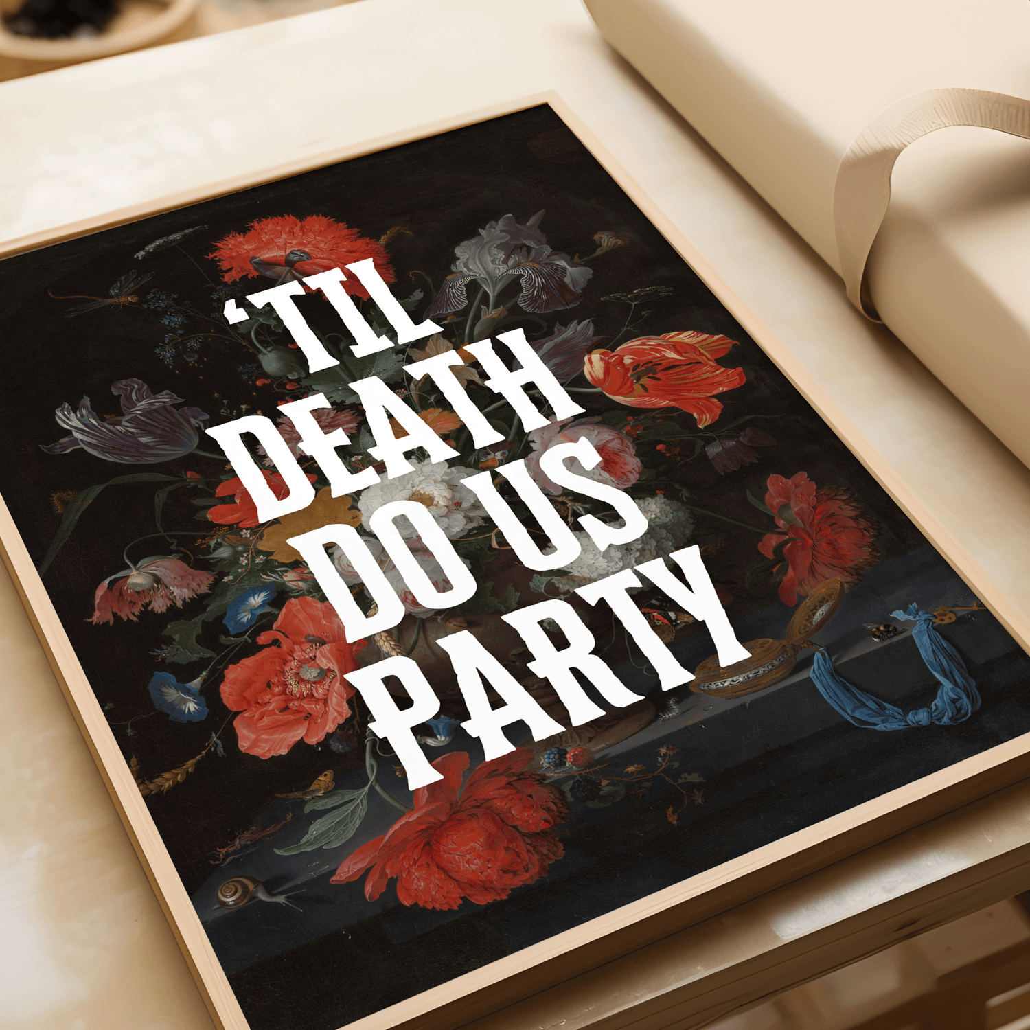 Framed artwork with dramatically dark,vintage floral design and text 'TIL DEATH DO US PARTY' on a table.