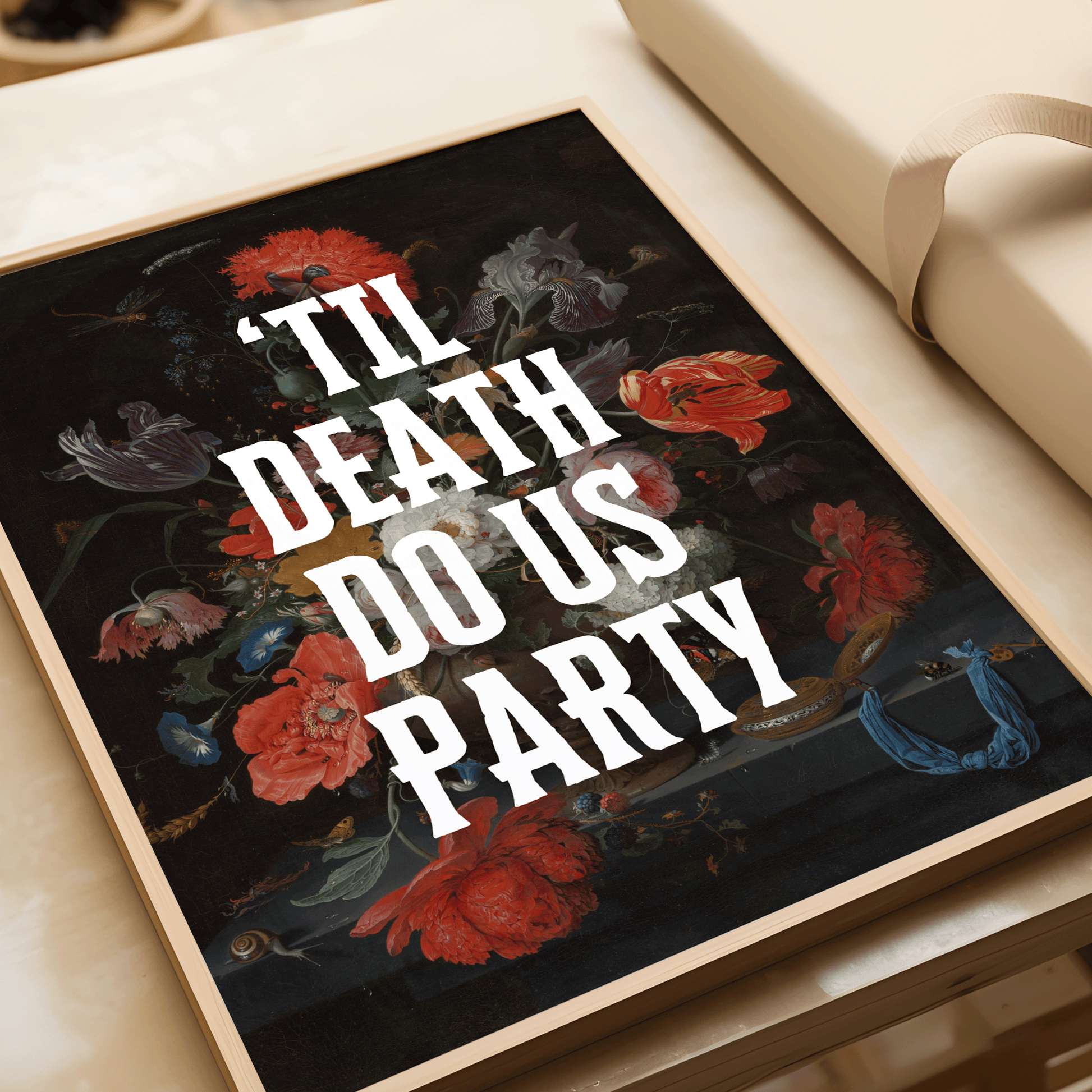 Framed artwork with dramatically dark,vintage floral design and text 'TIL DEATH DO US PARTY' on a table.